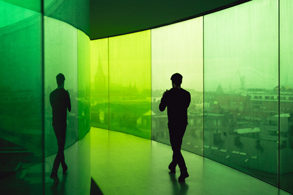 Man walking through a panoramic corridor with tinted glass walls in green and yellow tones, overlooking a cityscape.