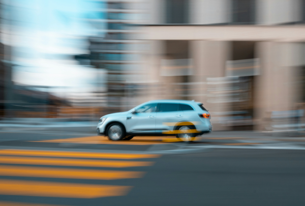 Weißer SUV mit getönten Scheiben fährt dynamisch durch die Stadt, Bewegungseffekt betont die Geschwindigkeit.