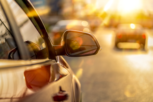 Getönte hintere Seitenscheibe eines Autos mit Sonnenschutzfolie, reflektierende Lichtstrahlen bei tiefstehender Sonne im Straßenverkehr.