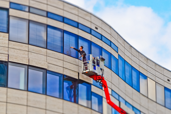 Specialist installs sun protection film on the windows of a modern office building with a lifting platform for optimum heat protection.